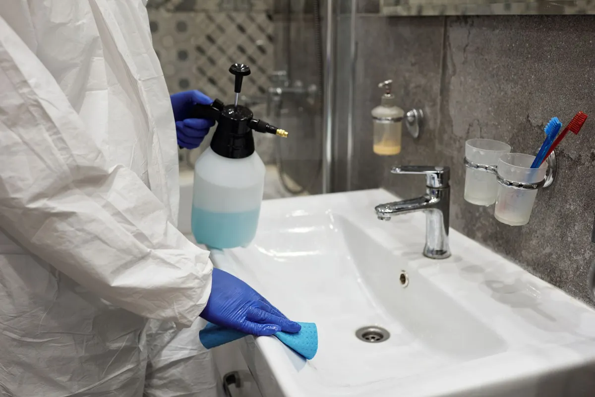 Gloved hand spraying and wiping a white bathroom sink