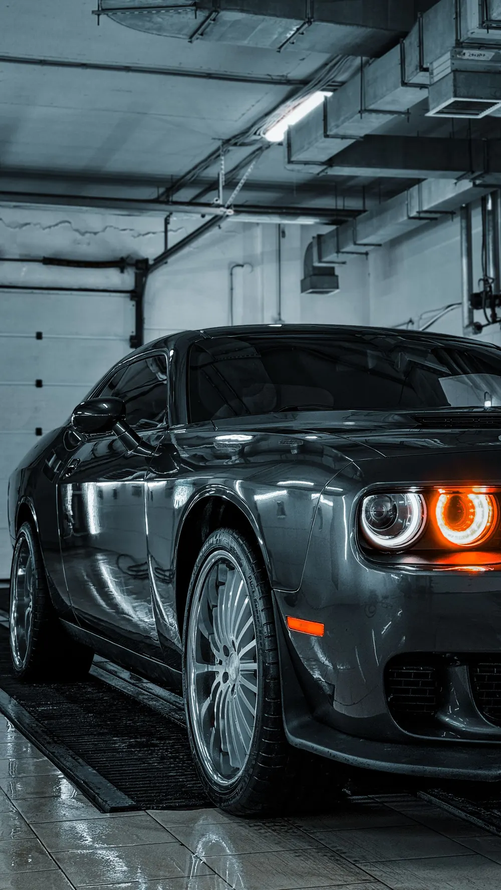 Glossy dark sports car with lit headlights in a garage