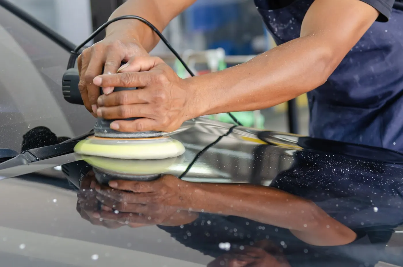 Hands guiding a machine polisher across glossy paint