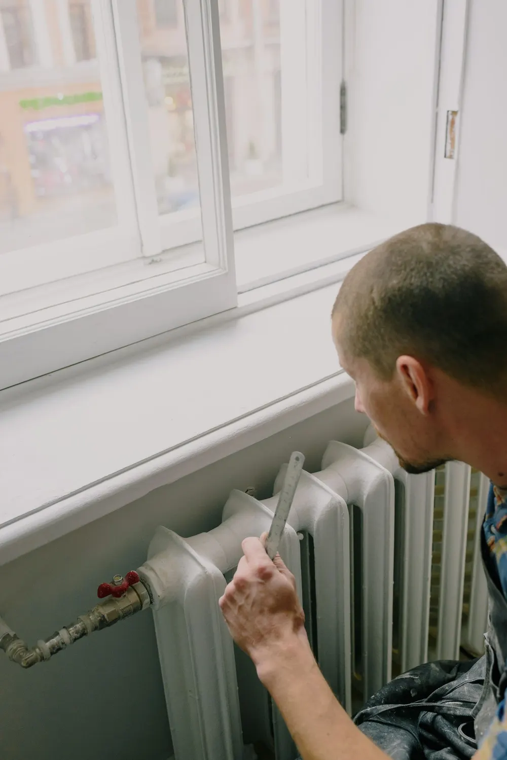 Technician checking a radiator beside a window