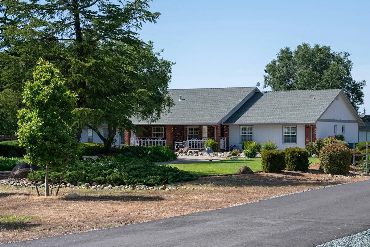 Ranch home with landscaped beds, shrubs, and mature trees