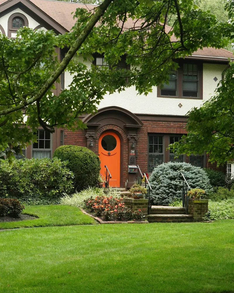Brick home with a red door, trimmed shrubs, and a green lawn