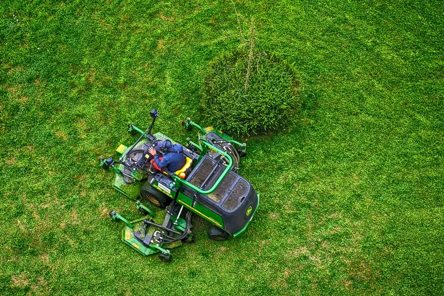 Ride-on mower cutting a green lawn, seen from above
