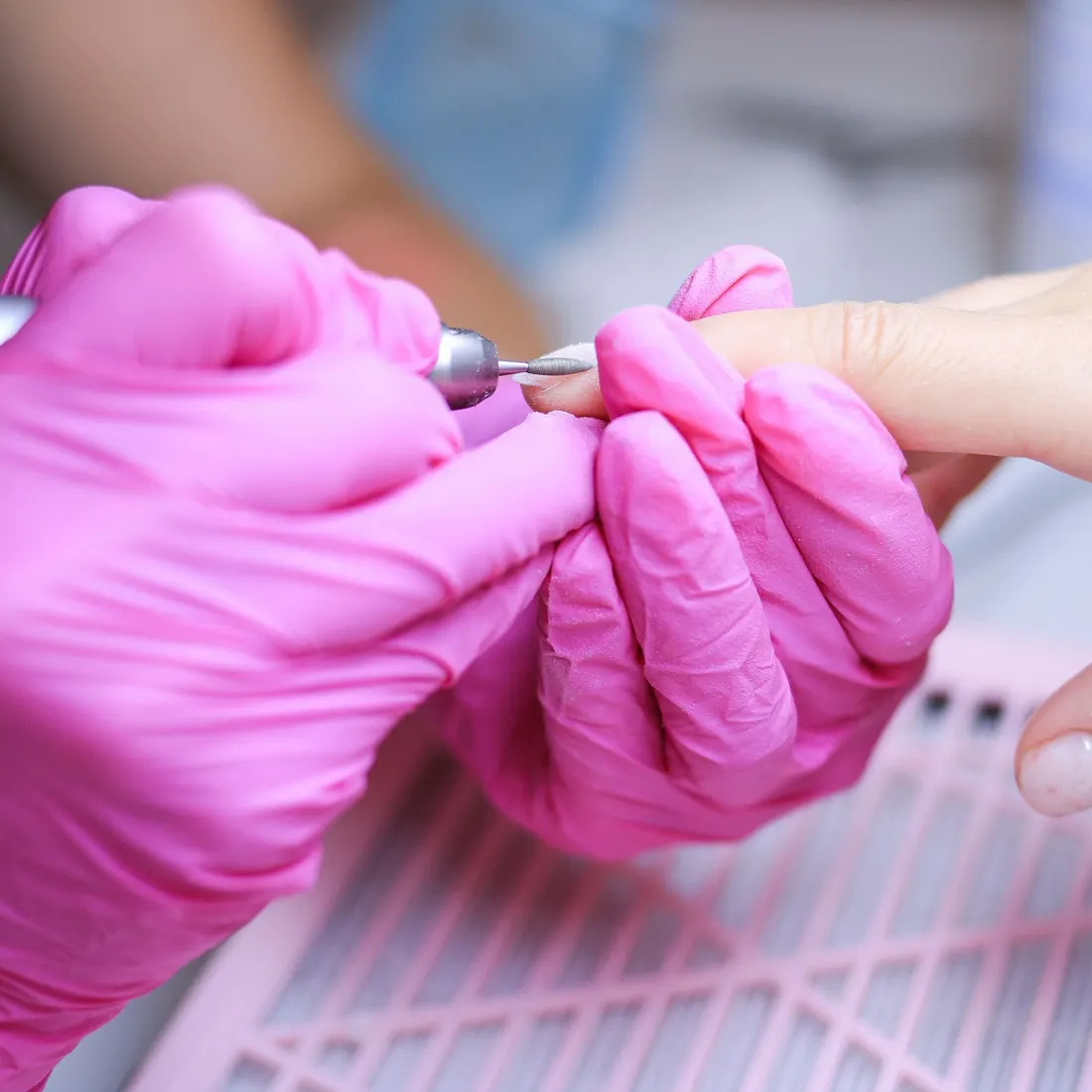 Technician in pink gloves refining a client's nail