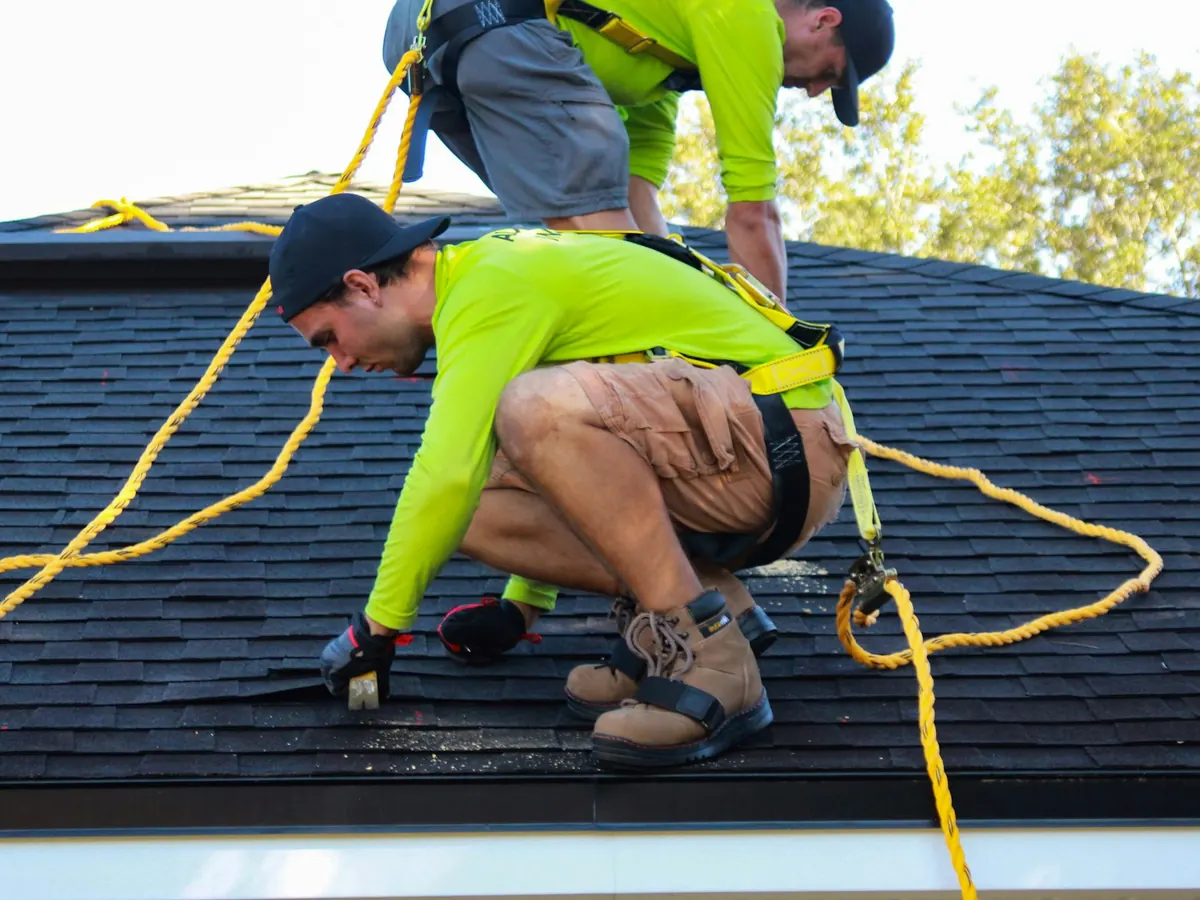 Roofer in safety harness installing shingles