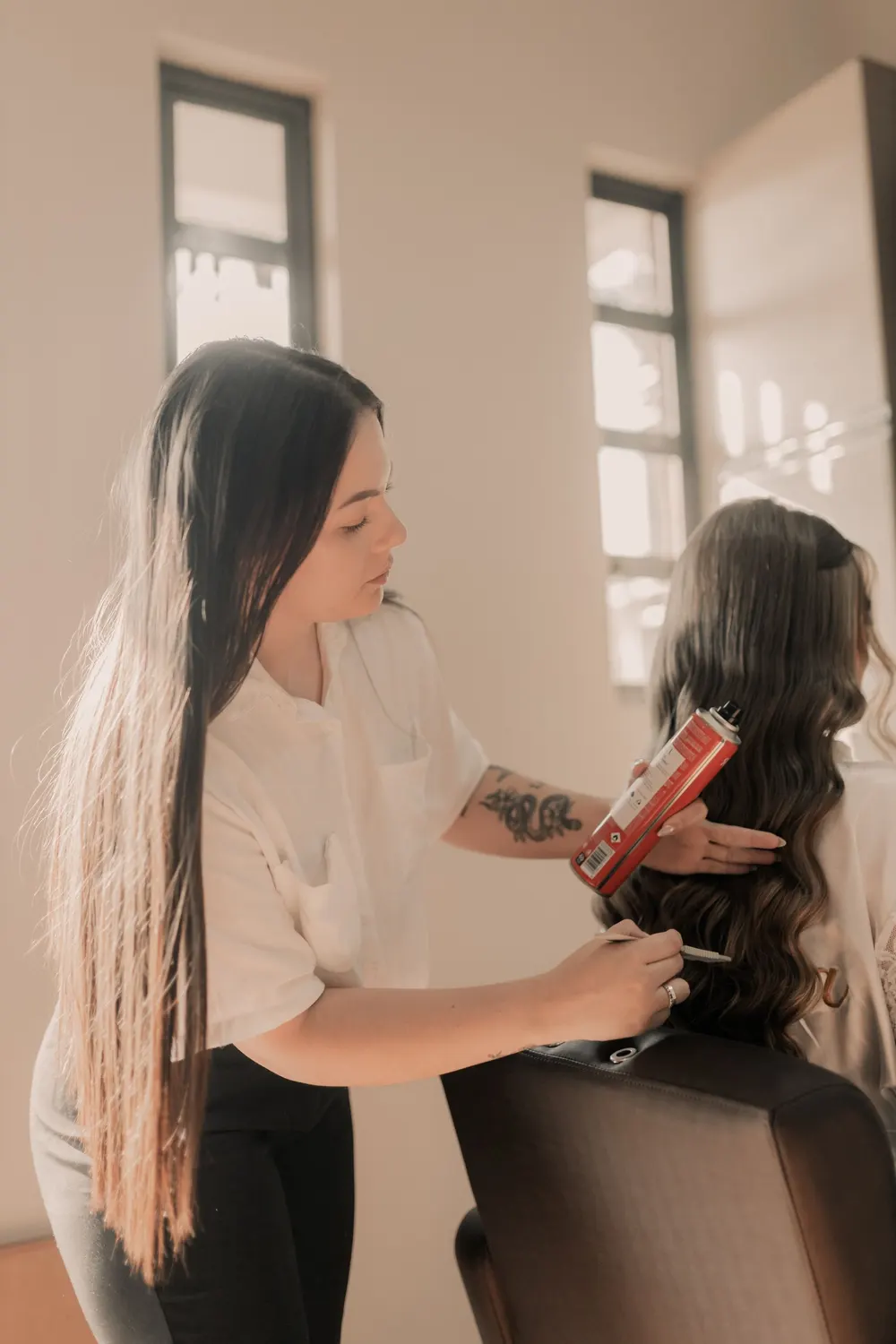 Stylist curling a client's long hair in a bright salon
