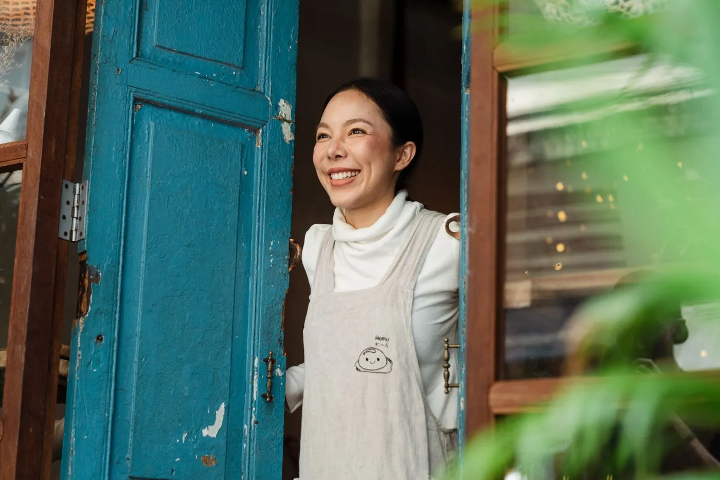 Café owner in an apron smiling at the door of her shop