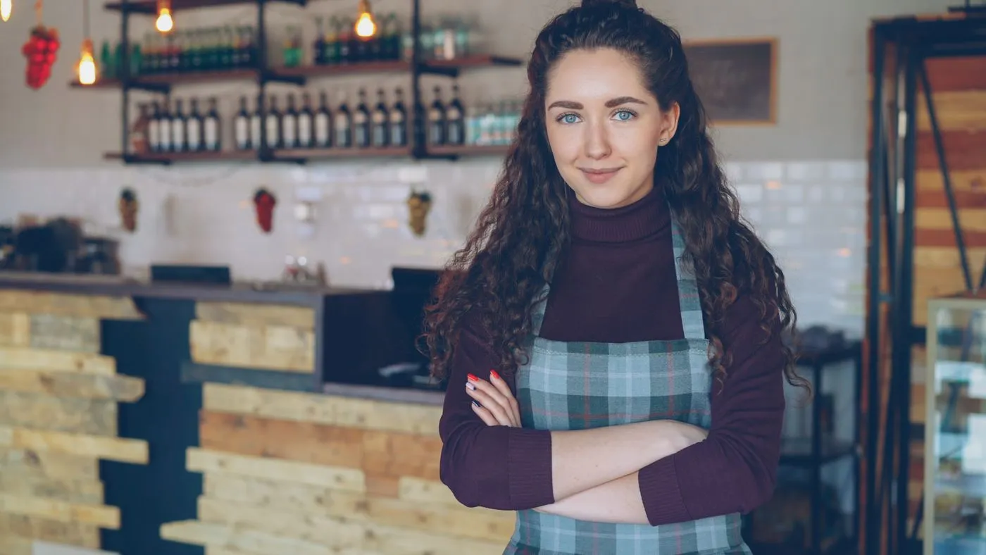 Confident café owner with arms crossed inside her coffee shop